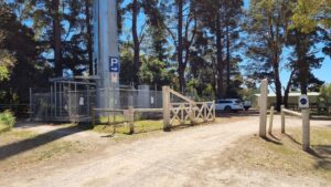 The car park entrance at Merricks with phone tower and replica level-crossing gate [2021]
